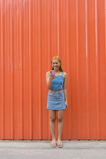 Full length shot of beautiful Asian girl with blonde hair against orange background