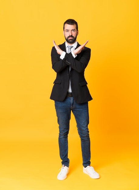 Full-length shot of business man over isolated yellow making NO gesture