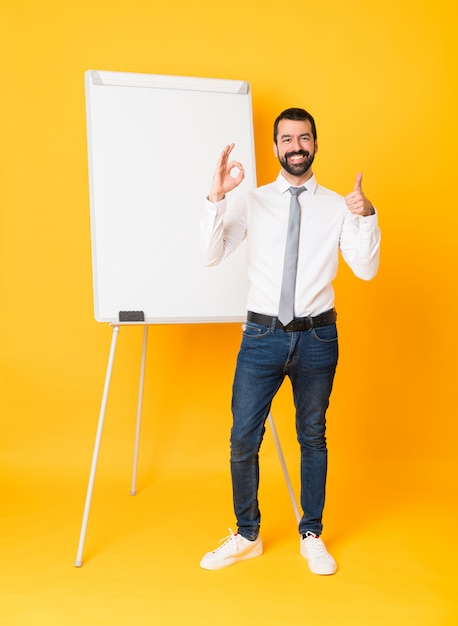 Photo full-length shot of businessman giving a presentation on white board over isolated yellow showing ok sign and thumb up gesture