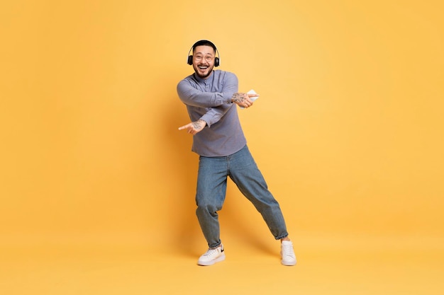 Full length shot of cheerful young asian man dancing on yellow background