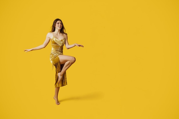 Full length shot of fashionable lady in golden elegant dress posing on yellow studio background free