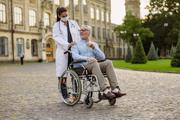 Full length shot of senior man handicapped patient in wheelchair smiling at young nurse in