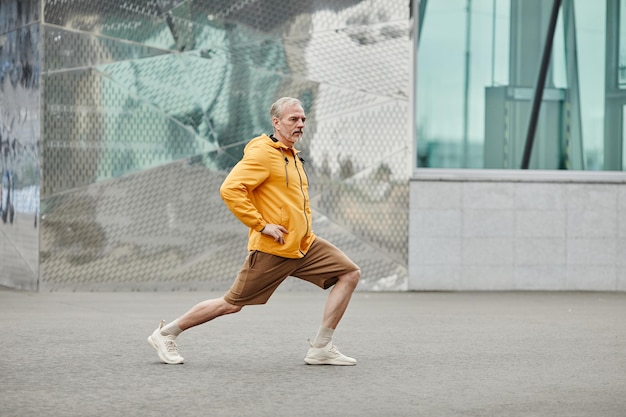 Full length side view portrait of handsome mature man stretching outdoors in urban city setting