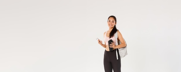 Full length of smiling healthy slim asian girl going fitness training female athelte carry backpack