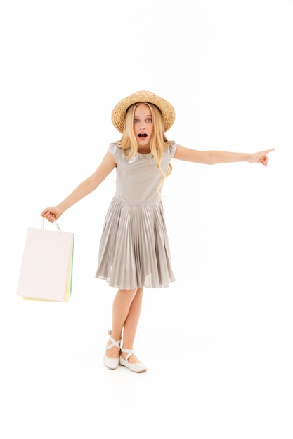 Full length Surprised young blonde girl in dress and straw hat looking at the camera while holding packages and looking away on white