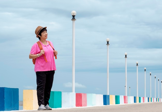 Full length view of Asian smiling female tourist looking sideways on bridge at sea viewpoint