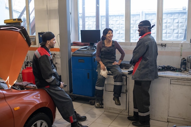 Full length view at diverse group of mechanics chatting during break in car repair shop