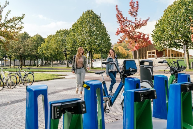 Full length view of two female friends approaching a bike rental station.