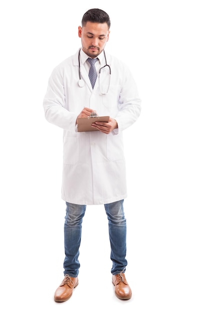 Full length view of a young male doctor taking some notes and recording his patient's history on a white background