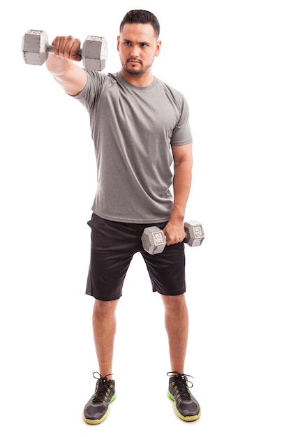 Full length view of a young man doing some deltoid raises with a couple of dumbbells on a white background