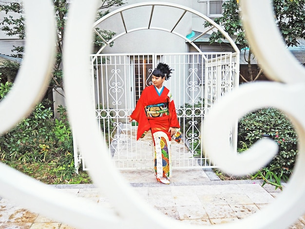 Photo full length of woman looking away while standing by gate seen through metal