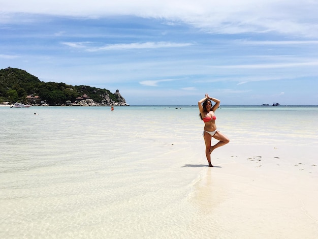 Photo full length of woman practicing yoga at beach against sky during summer