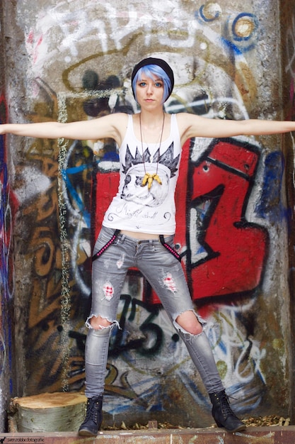 Photo full length of woman with arms outstretched in blue hair standing against graffiti wall