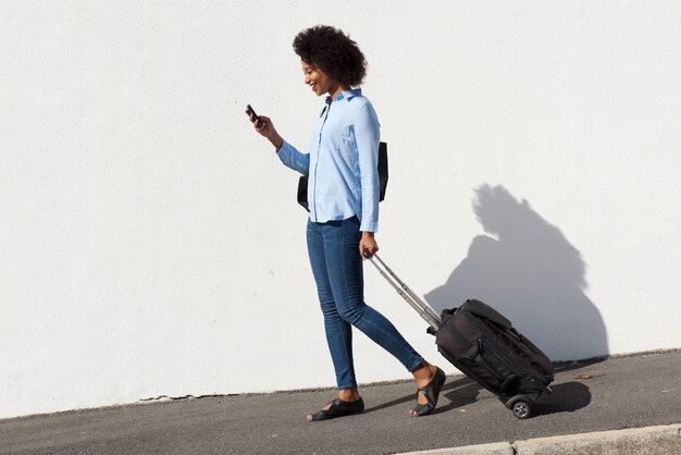 Photo full length young african woman walking with luggage and mobile phone