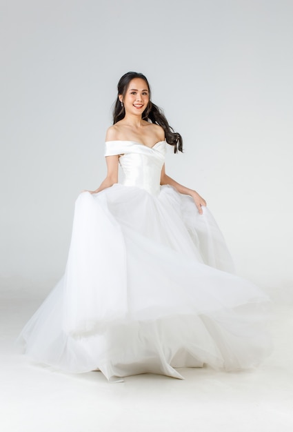 Full length of young attractive Asian woman, soon to be bride, wearing white wedding gown looking happy spinning. Concept for pre wedding photography.