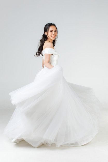 Full length of young attractive Asian woman, soon to be bride, wearing white wedding gown looking happy spinning. Concept for pre wedding photography.