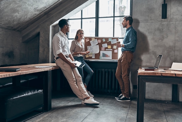 Full length of young coworkers in smart casual wear discussing business while working in office