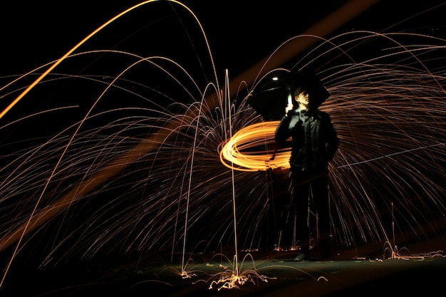 Photo full length of young man spinning wire wools while standing against sky at night