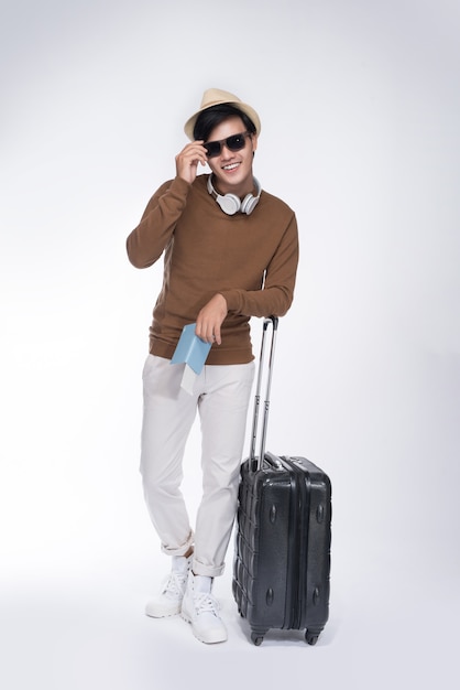 Full length of young tourist asian man holding passport with suitcase over grey background