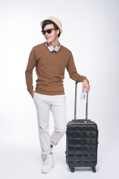 Full length of young tourist asian man holding passport with suitcase over grey background