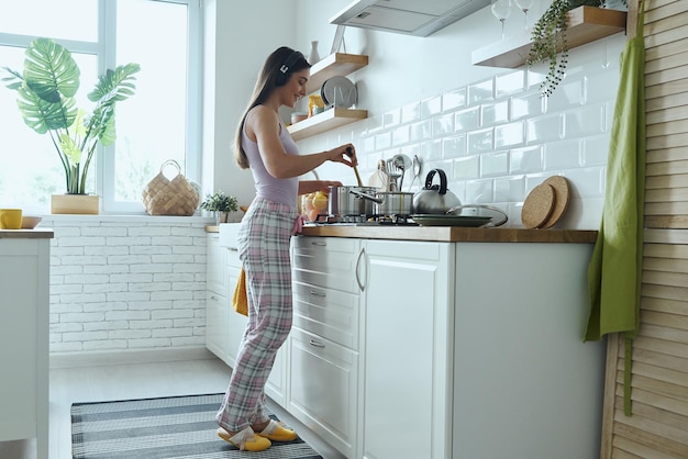 Full length of young woman in headphones enjoying music while cooking at the kitchen