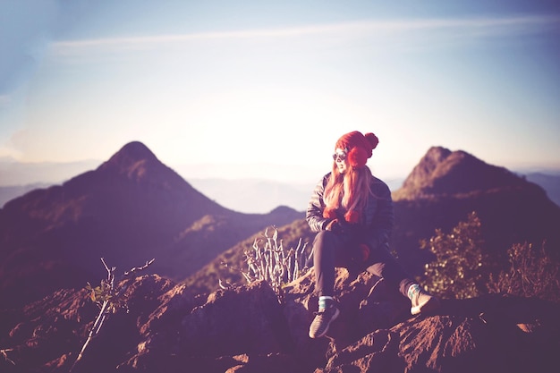 Full length of young woman sitting on rock formation against sky