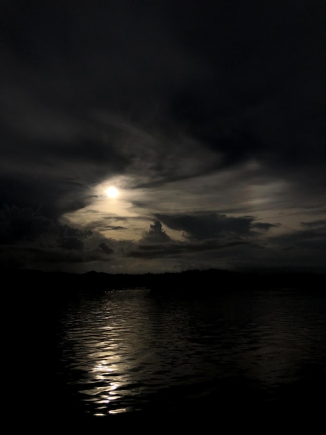 Photo a full moon is shining through the clouds over the water.