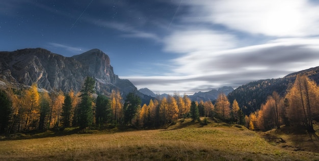 Full moon over the mountains in Dolomites alps at starry night in autumn Italian alps Colorful landscape with orange trees green meadow rocky mountains blue sky with stars and clouds in fall