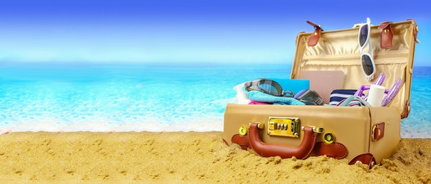 Full open suitcase on tropical beach background banner