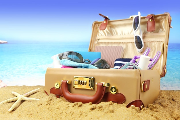 Full open suitcase on tropical beach background