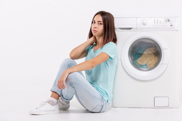 Full shot bored woman sitting near washing machine