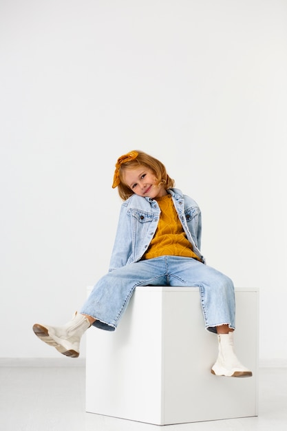 Full shot girl sitting on white cube