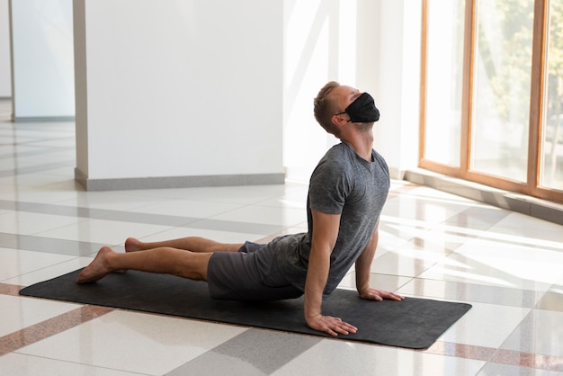 Full shot man wearing mask and doing yoga indoor