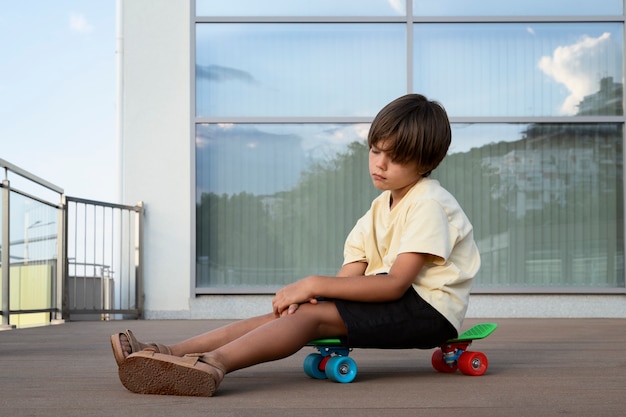 Full shot sad boy sitting on skateboard