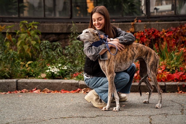 Full shot smiley woman hugging greyhound dog