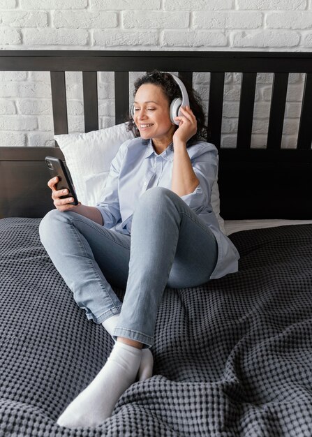 Full shot woman in bed with phone