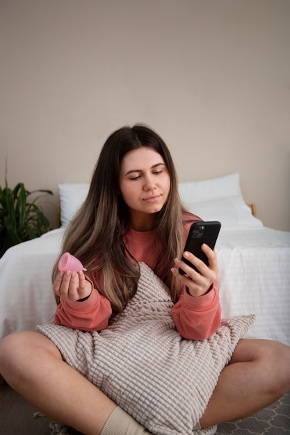 Full shot woman holding menstrual cup and phone