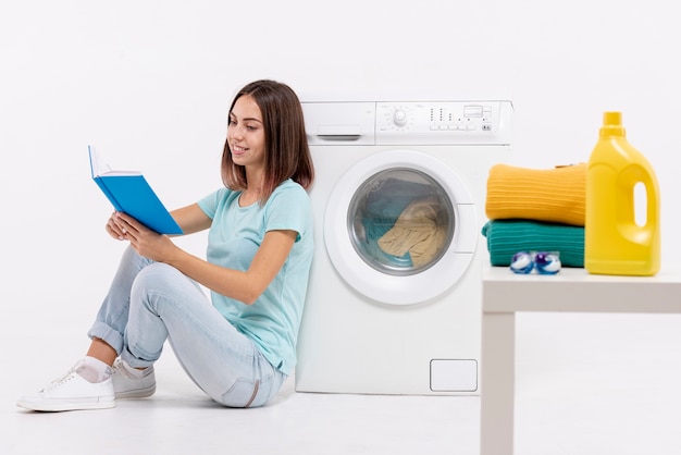 Full shot woman reading near washing machine