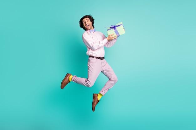 Full size photo of happy brunet hair young man jumping hold present wear formal outfit isolated on teal background