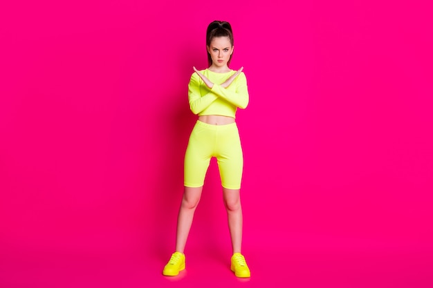 Full size photo of serious sportswoman cross arms show decline signal wear yellow short isolated on bright pink color background