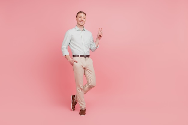 Full size photo of serious young man happy positive smile show peace cool v-sign confident isolated on pink color background