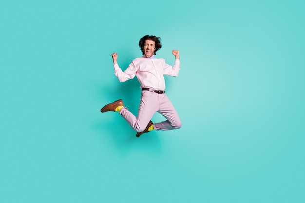 Full size portrait of happy crazy man scream yeah jump formal outfit yellow socks raise fists isolated on turquoise color background