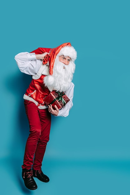 Full size of santa who claus carrying huge bag of presents while holding gift box in hand