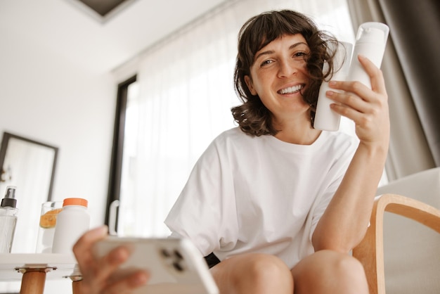 Full view of smiling woman with lotion doing selfie look at camera