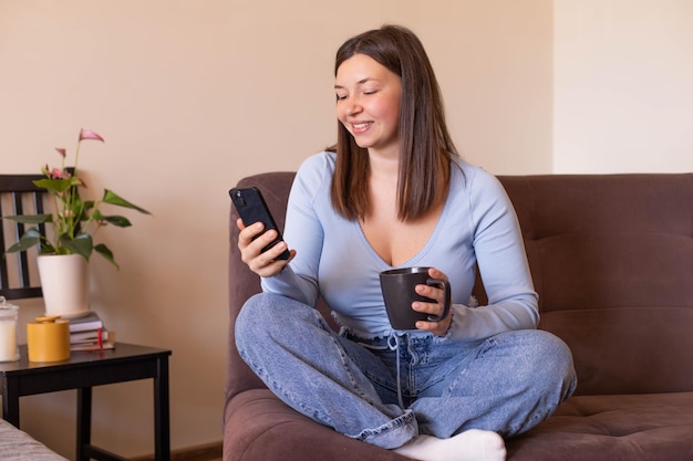 Full view of woman sitting at home look and smile at phone