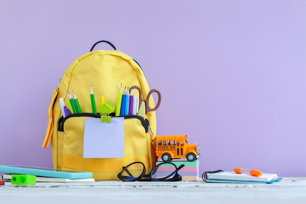 Full yellow school backpack with stationery on table on purple background