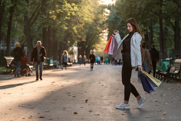 Fulllength portrait of young girl with colorful shopping bags in park background Woman shoped at shopping mall