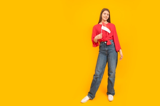 Fulllength portrait of young girl on yellow background Teenager holds the flag of Monaco or Indonesia