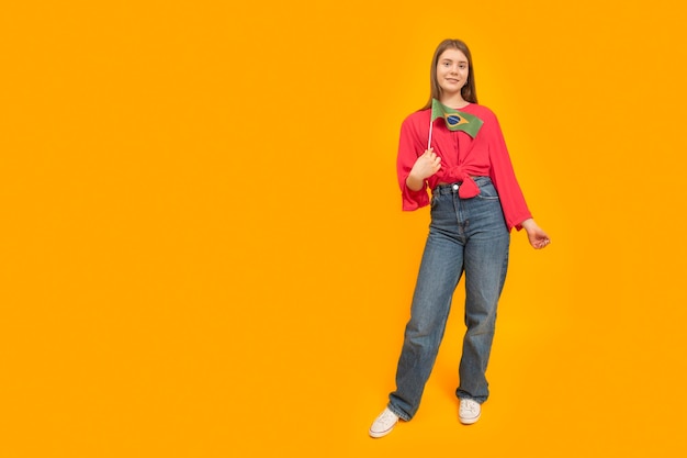 Fulllength portrait of young woman with Brazilian flag on orange background Girl holds flag of Brazil Copy space