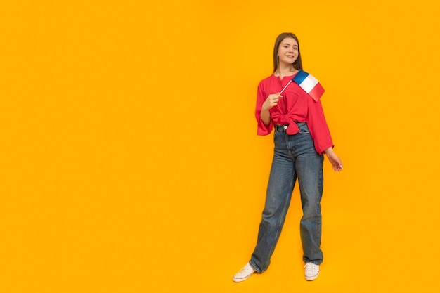 Fulllength portrait of young woman with the flag of France in her hands Yellow background Learn French Immigration to France